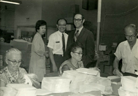 Workshop [Senior Work Center], Item 16, front: Dr. Bruce Douglas, IL state representative, visits the workshop. Foreground: Mary Ishibashi (far left), Namiye Suzuki (second from left). Standing: (from left) Pauline Yoshioka, Mr. Nambu, and Dr. Douglas