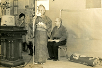 New Year's Party, Item 18, front: Mrs. Monma at the microphone