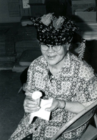 Blood Assurance, Communal Living, Issei Work Center, Body Dynamics, Annual Community Picnic, and Market Day, Item 16, front: Mrs. Monma models her Easter Parade hat. Participants made hats and ties from materials available in the work center.